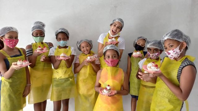 Crianças de avental e touca mostrando o que prepararam em oficina de culinária