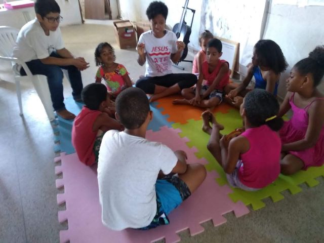 Crianças e voluntários em roda de conversa sobre tapete colorido