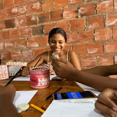 Voluntária sorrindo durante oficina, sentada a uma mesa de tijolos aparentes